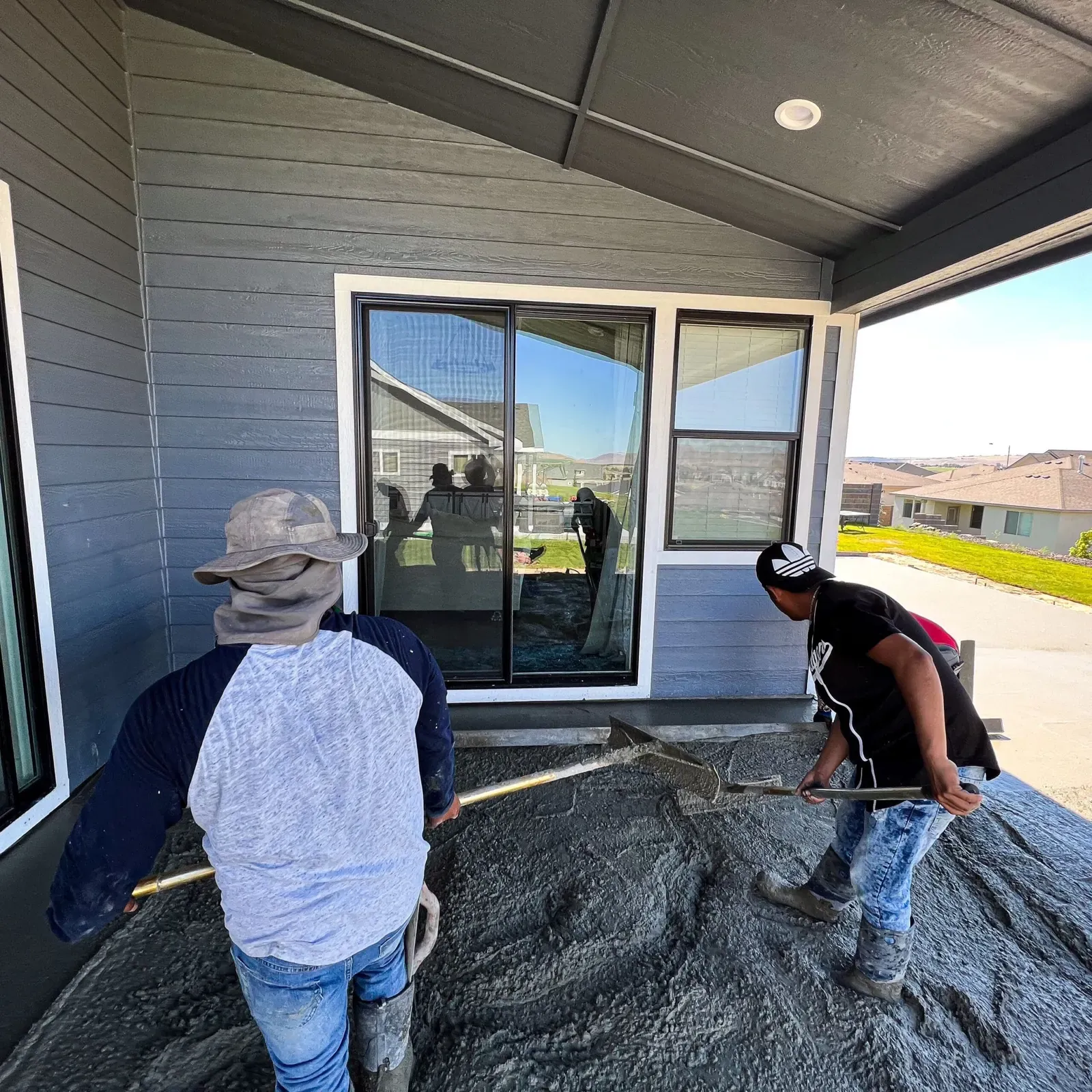 Crew hand-finishing a covered patio pour at a new home