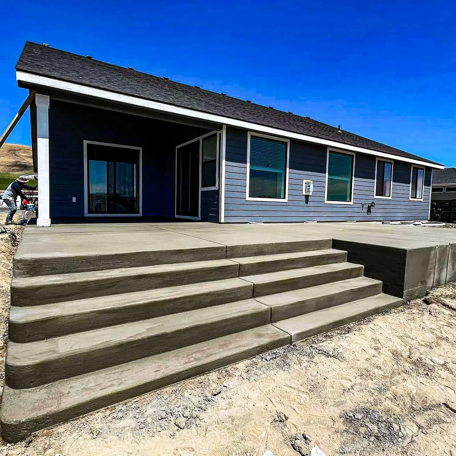 Wraparound concrete steps and porch freshly poured at a blue home