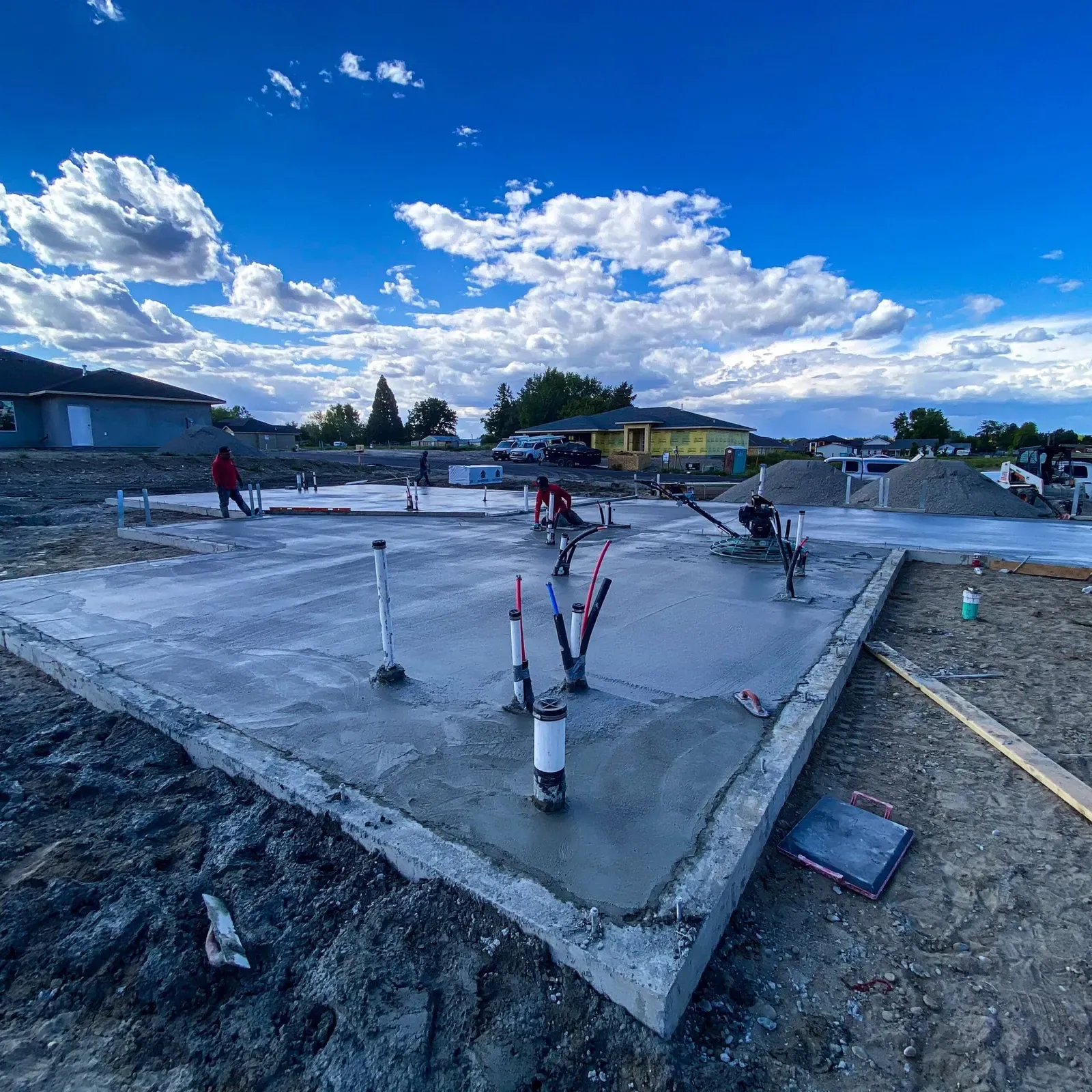 Crew power-troweling a large slab foundation with plumbing stub-outs