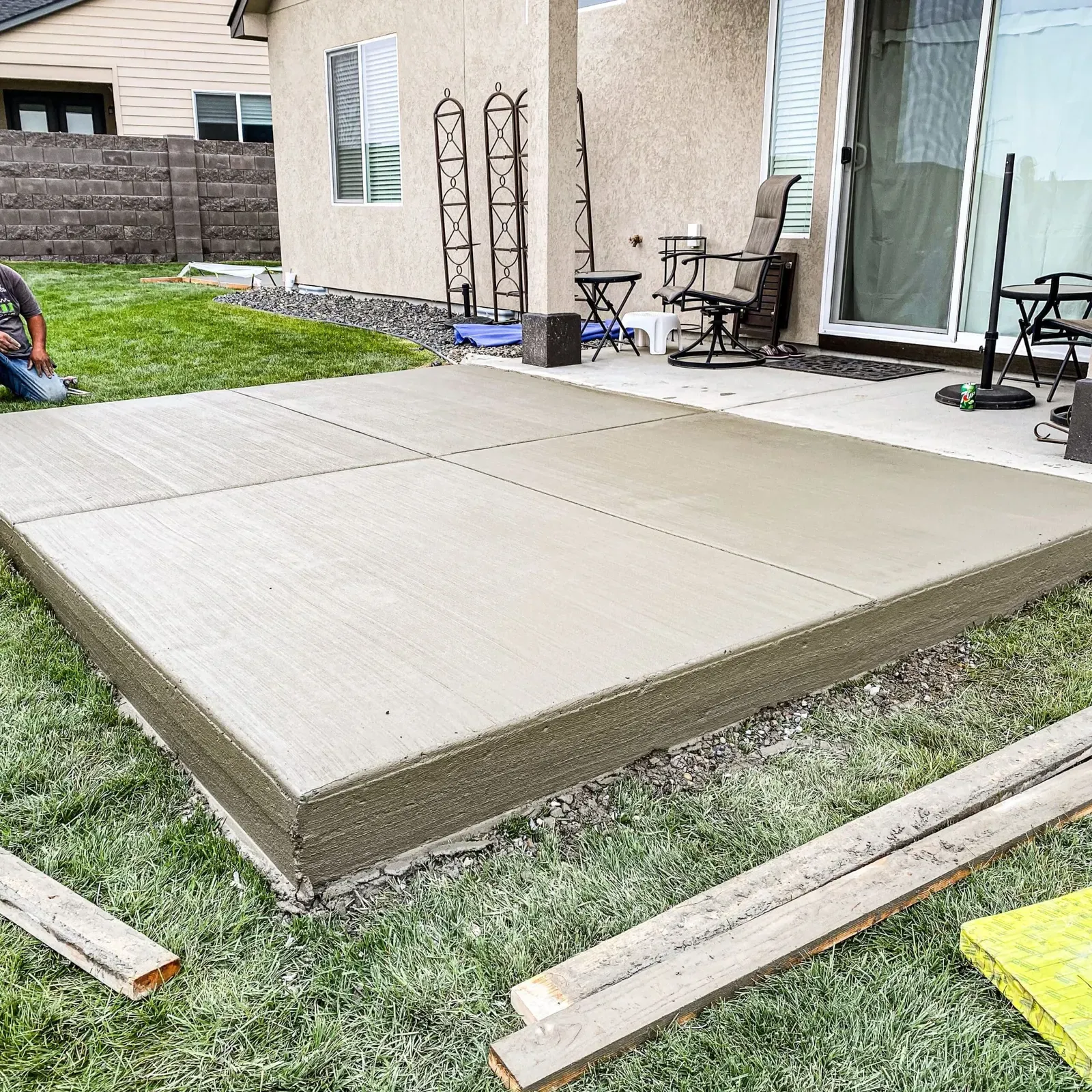 New square concrete patio pad set into a green backyard lawn