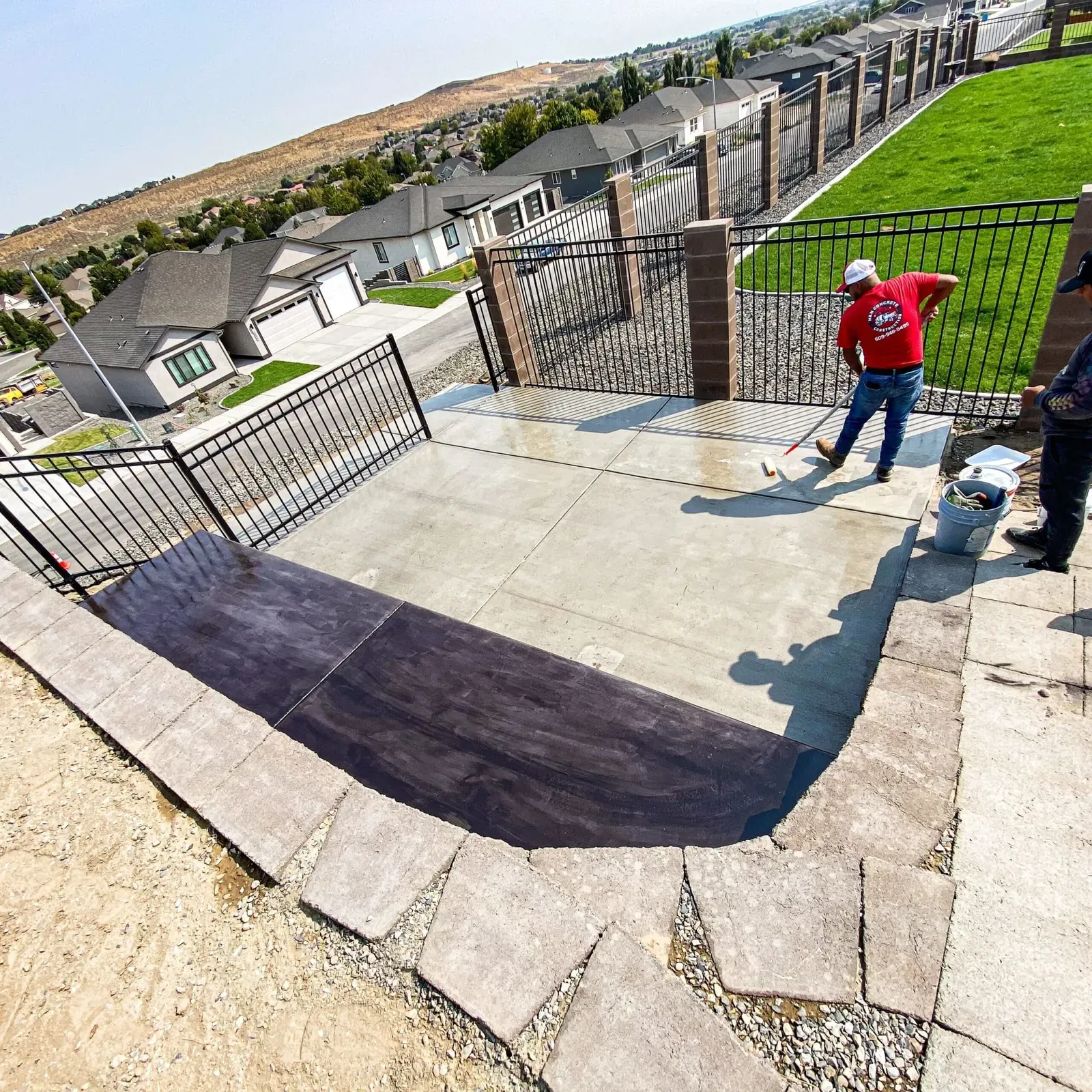 Crew sealing a decorative dark border on a new concrete patio