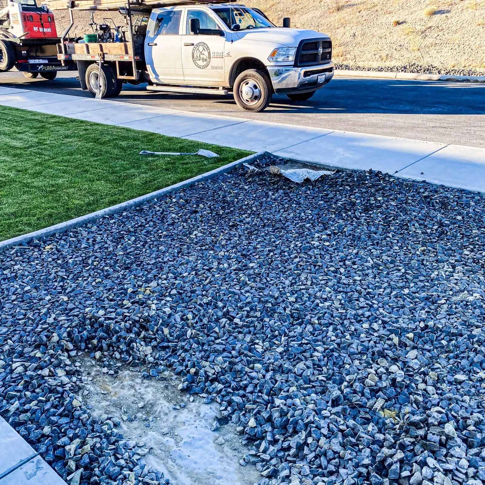 Compacted gravel base prepped beside a finished sidewalk, work truck behind