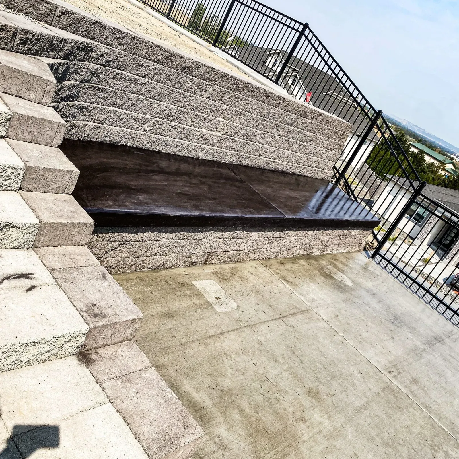 Sealed concrete patio in a dark finish beside a block retaining wall