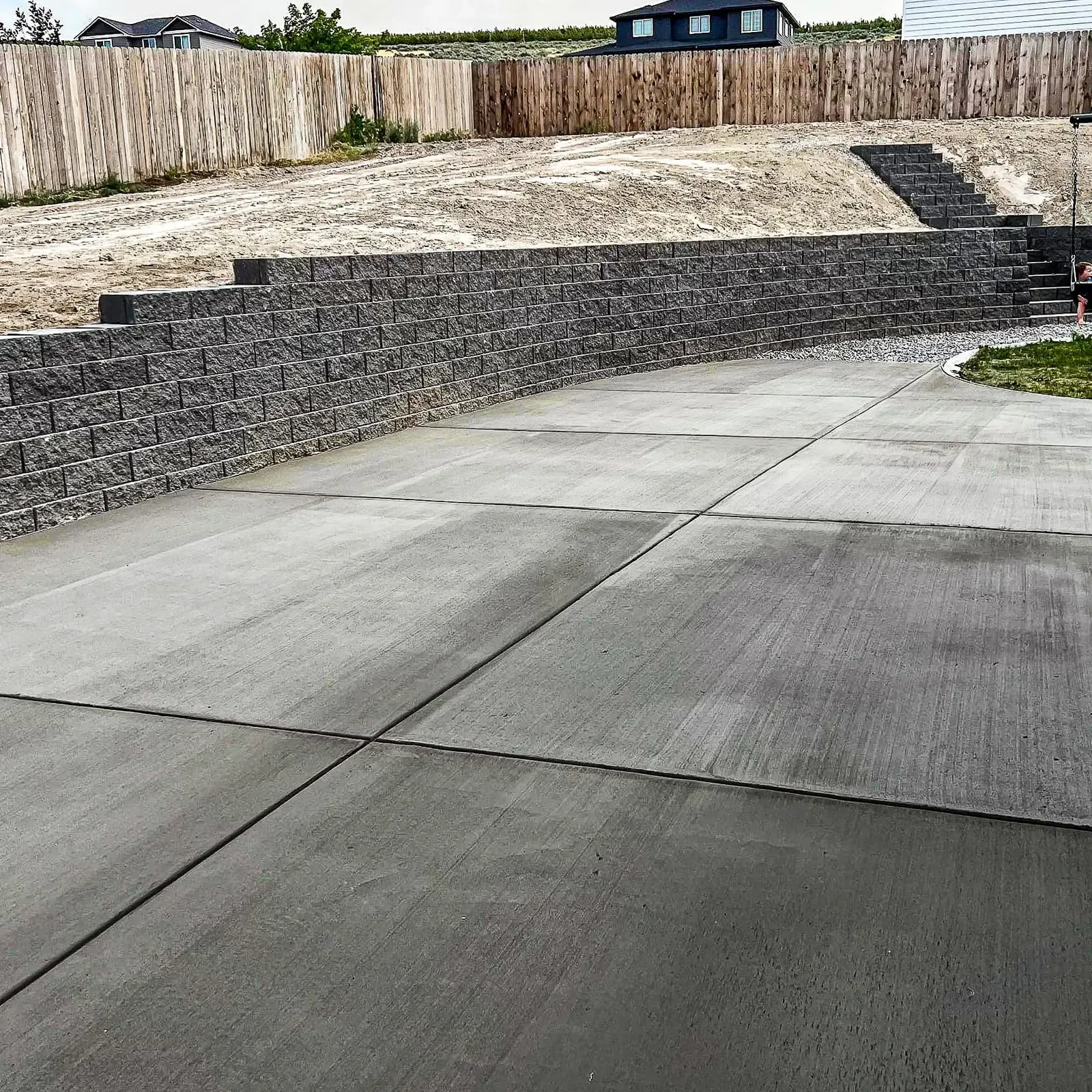 Broom-finished new driveway below a block retaining wall