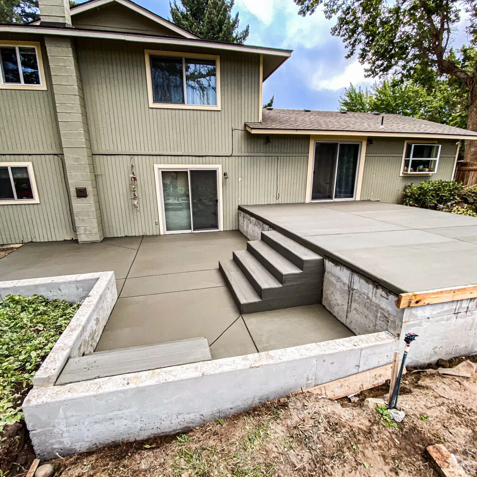 Raised backyard patio with new concrete steps at a split-level home